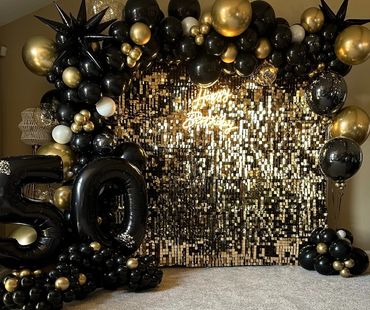 Black and gold balloon decoration with a '50' and shiny backdrop for a birthday.