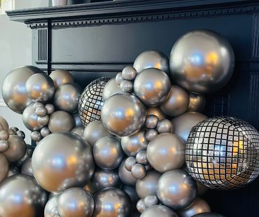 A cluster of metallic silver balloons with two disco ball balloons.