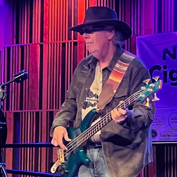 Musician playing bass guitar on stage wearing a black hat.
