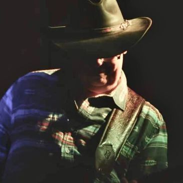 Man in a hat playing guitar in dim light.