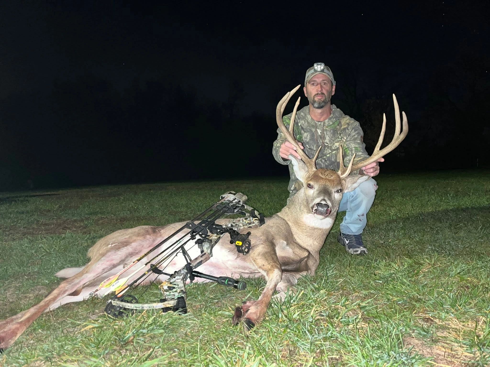 Hunter poses with a large buck and bow at night.