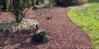 A landscaped garden bed with red mulch and green grass.