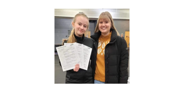 A skater holding test forms and posing with a coach