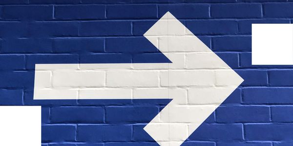 Large white arrow painted on blue brick wall, symbolising direction, momentum, and forward movement.