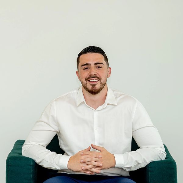 Man in white shirt and blue pants sitting on green chair, smiling.