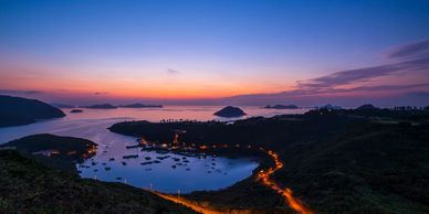 Sunset over a coastal bay with islands and illuminated roads.