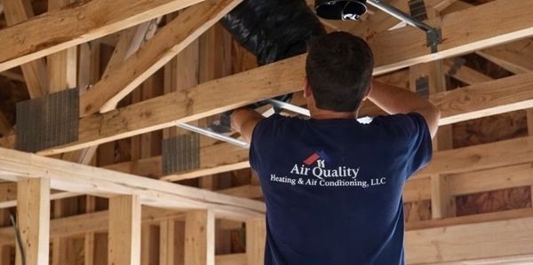 Technician installing HVAC ducts in a house under construction.