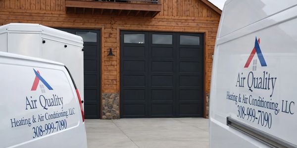 Two Air Quality Heating & Air Conditioning vans parked in front of a wooden house.