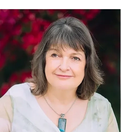 Smiling middle-aged woman with shoulder-length hair and pendant necklace.