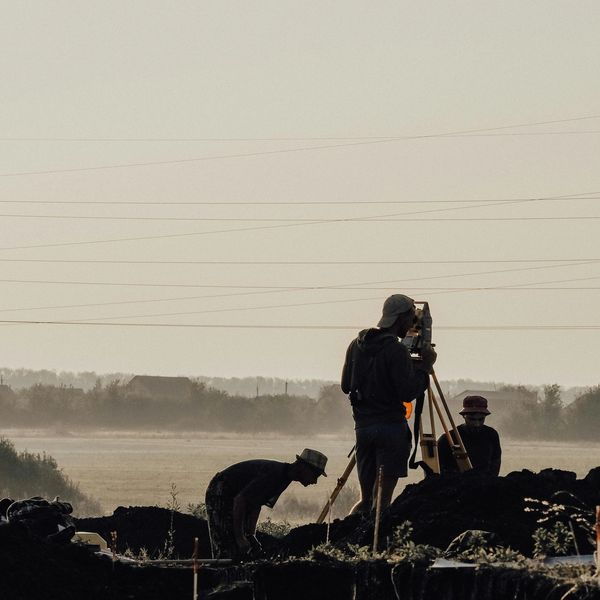Personas trabajando al amanecer en campo con equipo de topografía