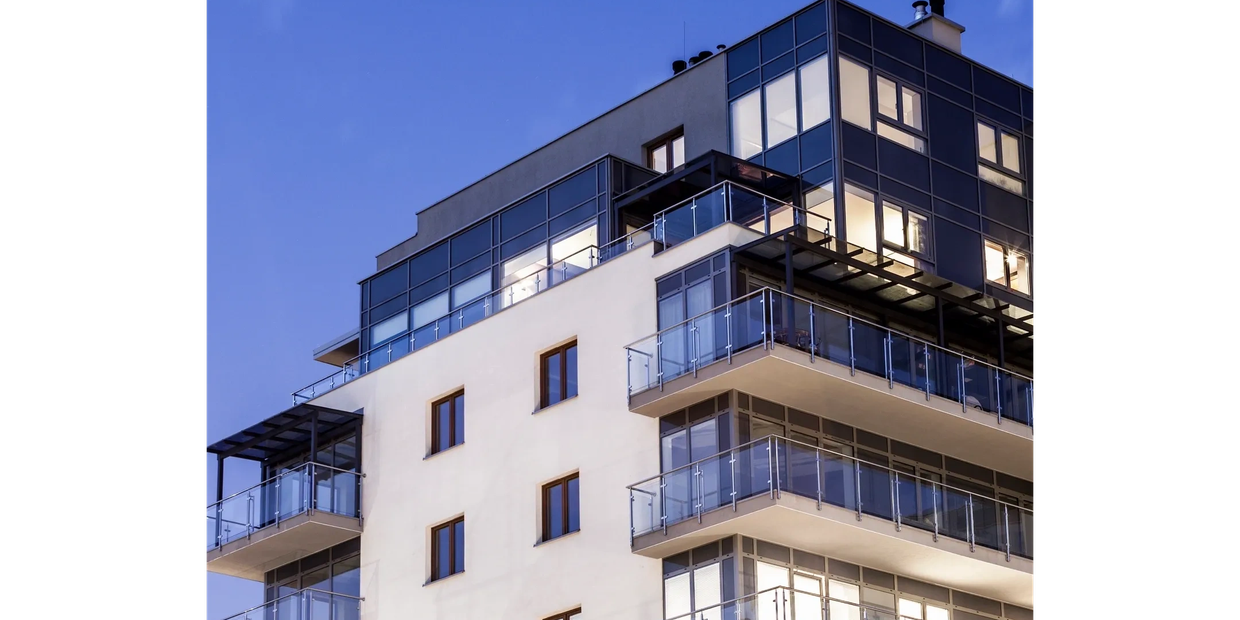 Modern apartment building with glass balconies against a clear evening sky.