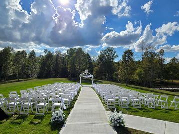 Outdoor wedding setup with white chairs and a decorated arch.