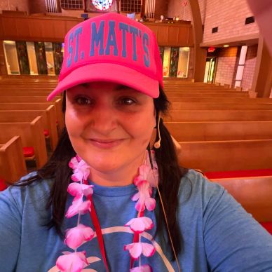 Woman smiling in a church wearing a pink hat and lei.