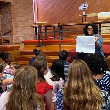 A woman reads to children gathered on the floor inside a church.
