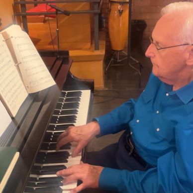 Elderly man playing piano with sheet music.