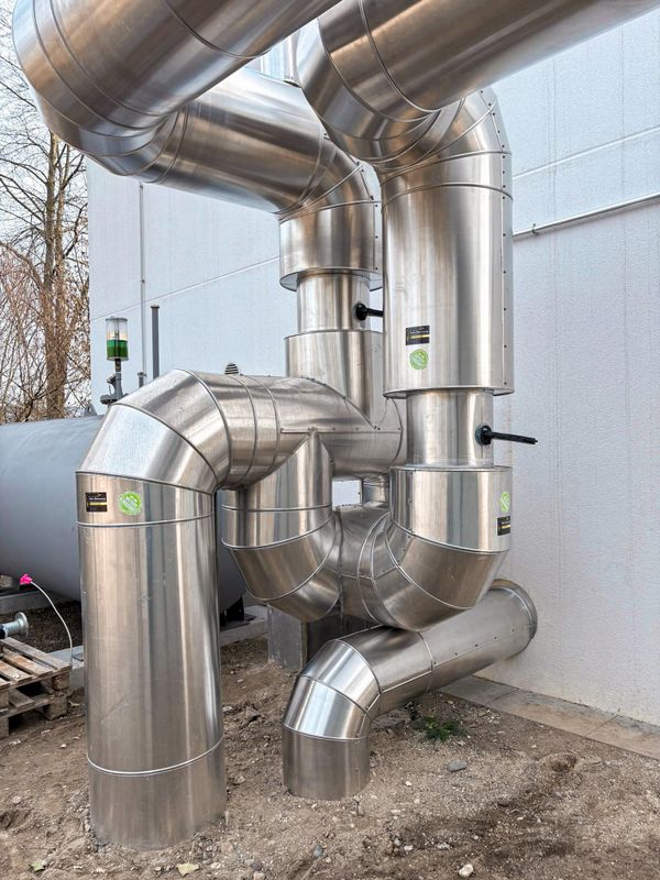 Complex stainless steel industrial piping system outdoors near a building.