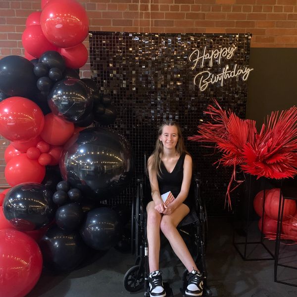 Young woman in wheelchair at a birthday party with black and red balloons.