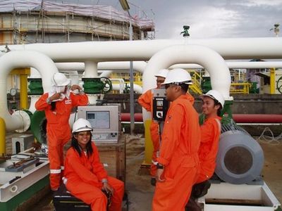 Workers in orange safety gear at an industrial plant with large pipes.