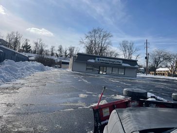 Plowed snowy parking lot with a small business building and clear blue sky.