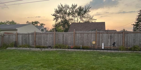 A backyard with a wooden fence and green grass at sunset.