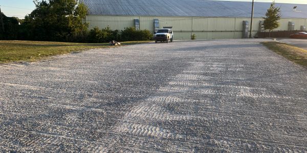 Empty gravel parking lot with a single truck and a building in the background.