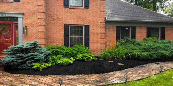 Well-maintained garden with lush greenery and fresh mulch outside a brick house.