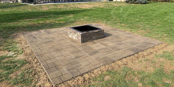 A square stone fire pit area on a grassy lawn.