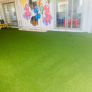 Indoor play area with artificial green turf and colorful wall decor.