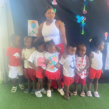 A group of young children standing with a woman against a decorated black backdrop.