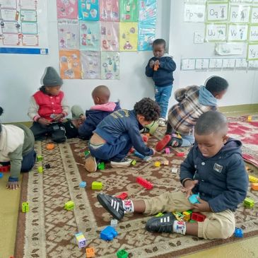 Young children playing with colorful blocks on a carpet in a classroom.