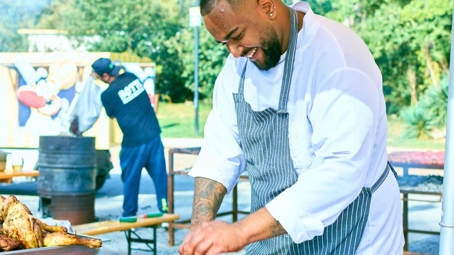 Chef joyfully prepares grilled chicken at an outdoor event on a sunny day.