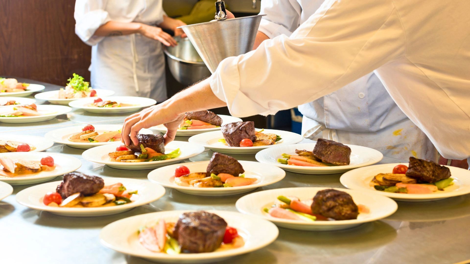 Chefs plating gourmet steak dishes in a busy kitchen.