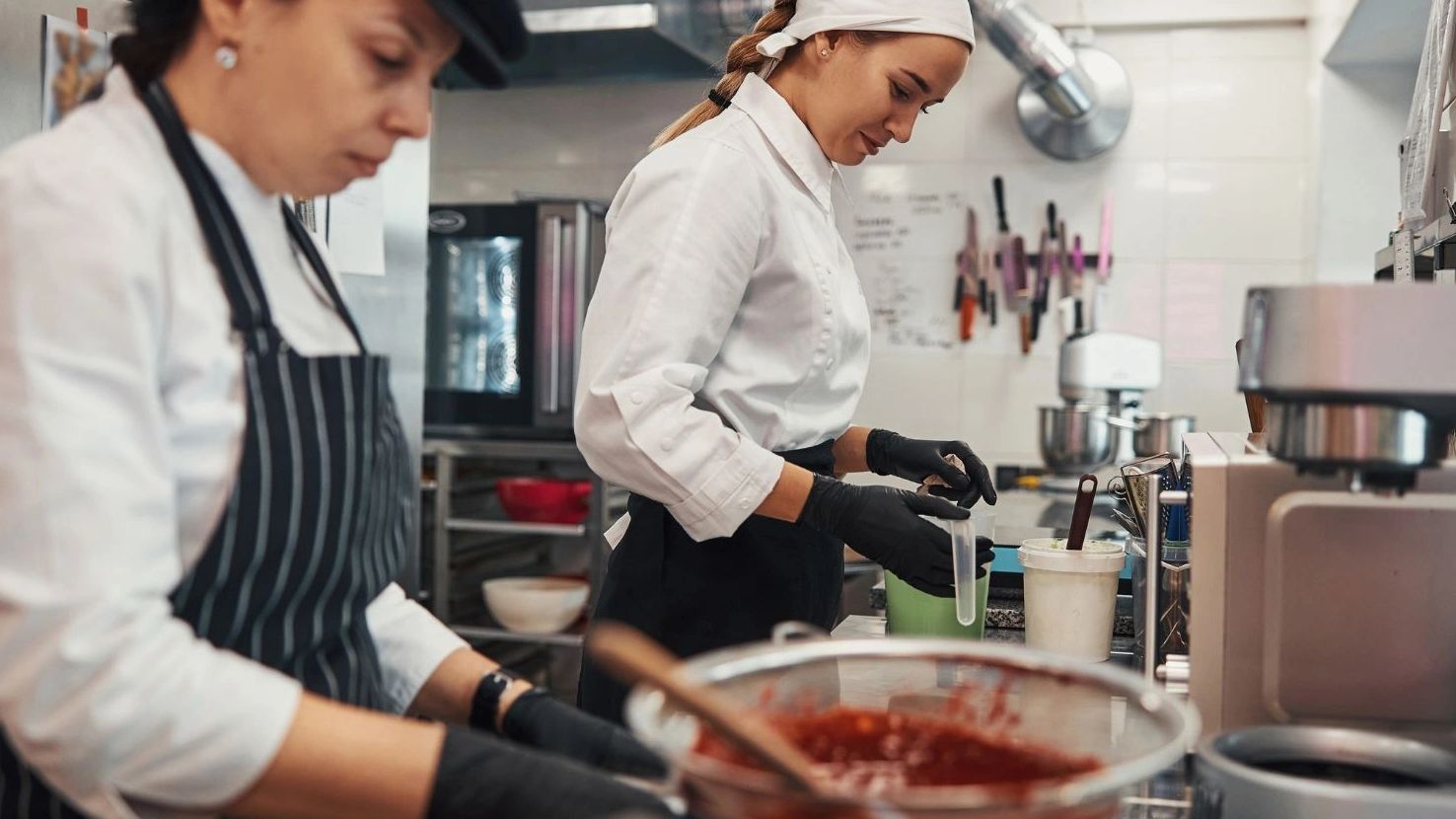 Two chefs preparing food in a professional kitchen with focused expressions.