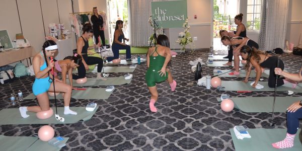 Group yoga or fitness class indoors with participants using poles and pink balls.