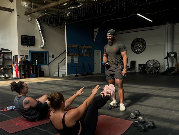 Two women exercising on mats with a smiling male trainer in a gym.