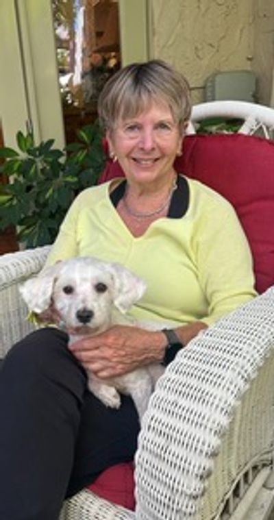 Woman sitting on a wicker chair with a small white dog.