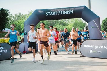 Runners begin a race under a start/finish arch on a sunny day.