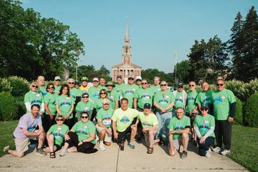 Group of people in green shirts posing outdoors in front of a building with a spire.