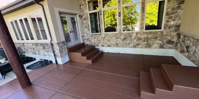 Brown deck with steps and stone wall house exterior.