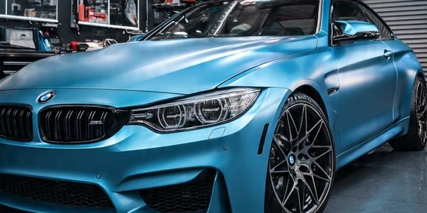 Close-up of a matte blue BMW with black rims in a garage.