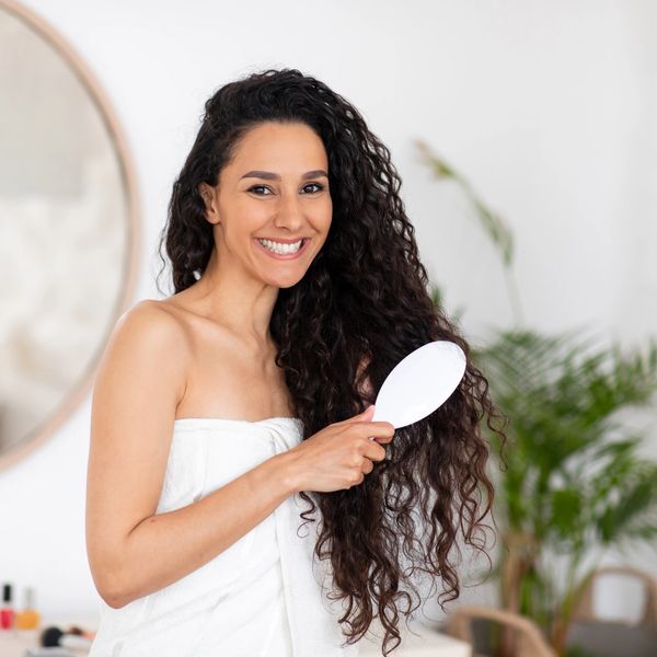 FEMALE COMBING HER LONG DARK CURLY HAIR PREPARING FOR A CURLY HAIR CONSULTATION