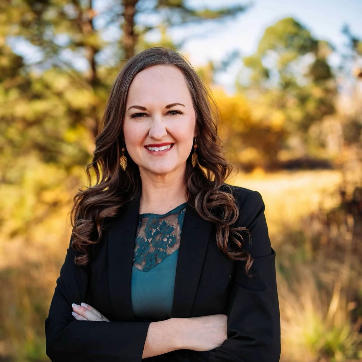 Confident woman in black blazer smiling outdoors in autumn.