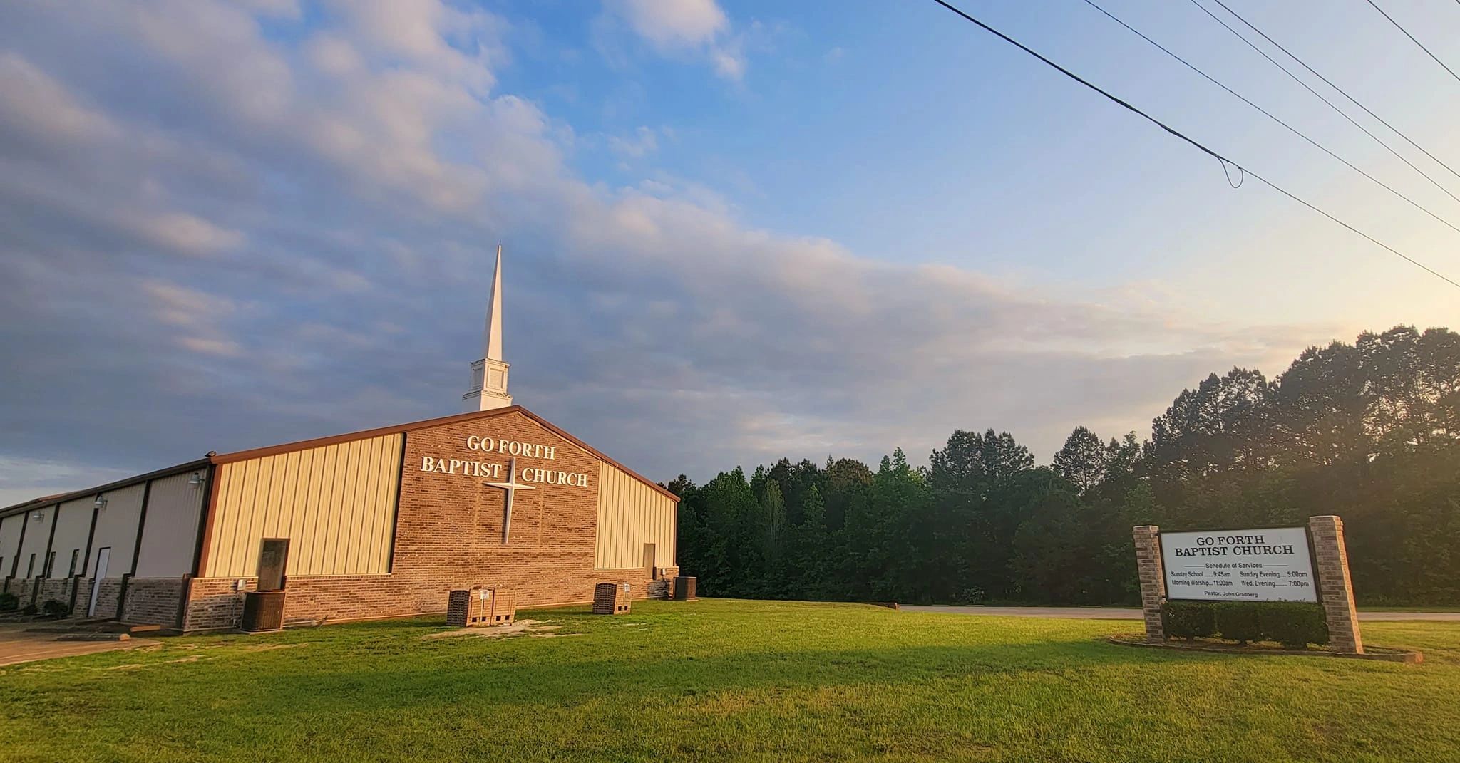 Go Forth Baptist Church building with a sign and green lawn under a cloudy sky.