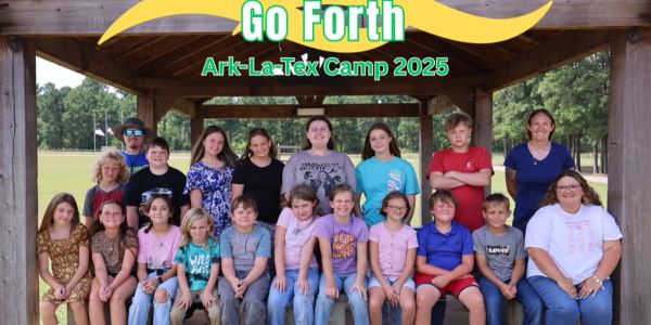 Group photo of kids and adults at Ark-La-Tex Camp 2025 under a wooden shelter.