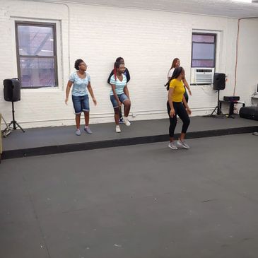 Group of young women dancing on a small stage indoors.