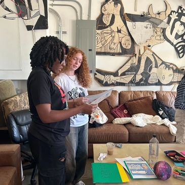 Three people engaged in a discussion or review of documents in a cozy room with artwork on the walls.