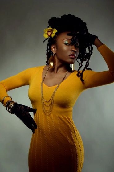 Confident woman in mustard yellow dress with black gloves and flower in hair.