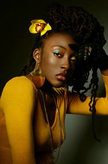 Elegant woman with dreadlocks wearing mustard yellow and a yellow flower in her hair.
