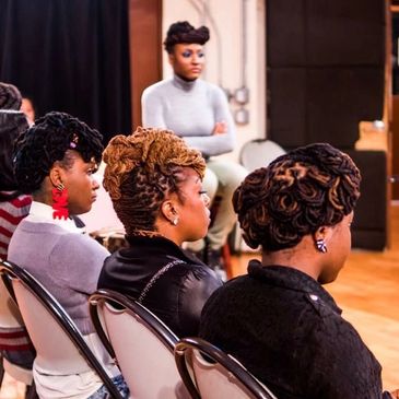 Women with intricate braided hairstyles seated attentively in a room.