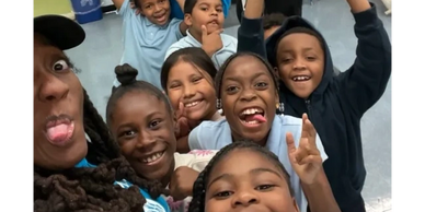 A group of children and an adult making funny faces and smiling for a selfie indoors.